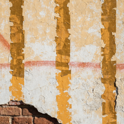 A sun-bleached plaster wall with four dark vertical tape shadows, a faded spray fade running across it and a corner of exposed brick.