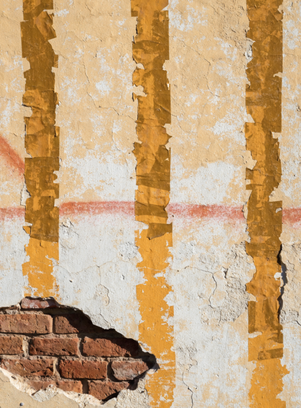 EMRWHwPtu2kfgbGrBNOBp_uq7HJw0Z.webp A sun-bleached plaster wall with four dark vertical tape shadows, a faded spray fade running across it and a corner of exposed brick.