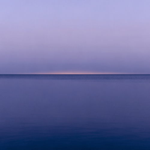 Tb3oTjJE6YR6djvbyHEOW_wcigX4p0.webp A minimalist Nordic scene of a low, level horizon with pale gold light meeting cold blue above still, flat water and an empty sky.